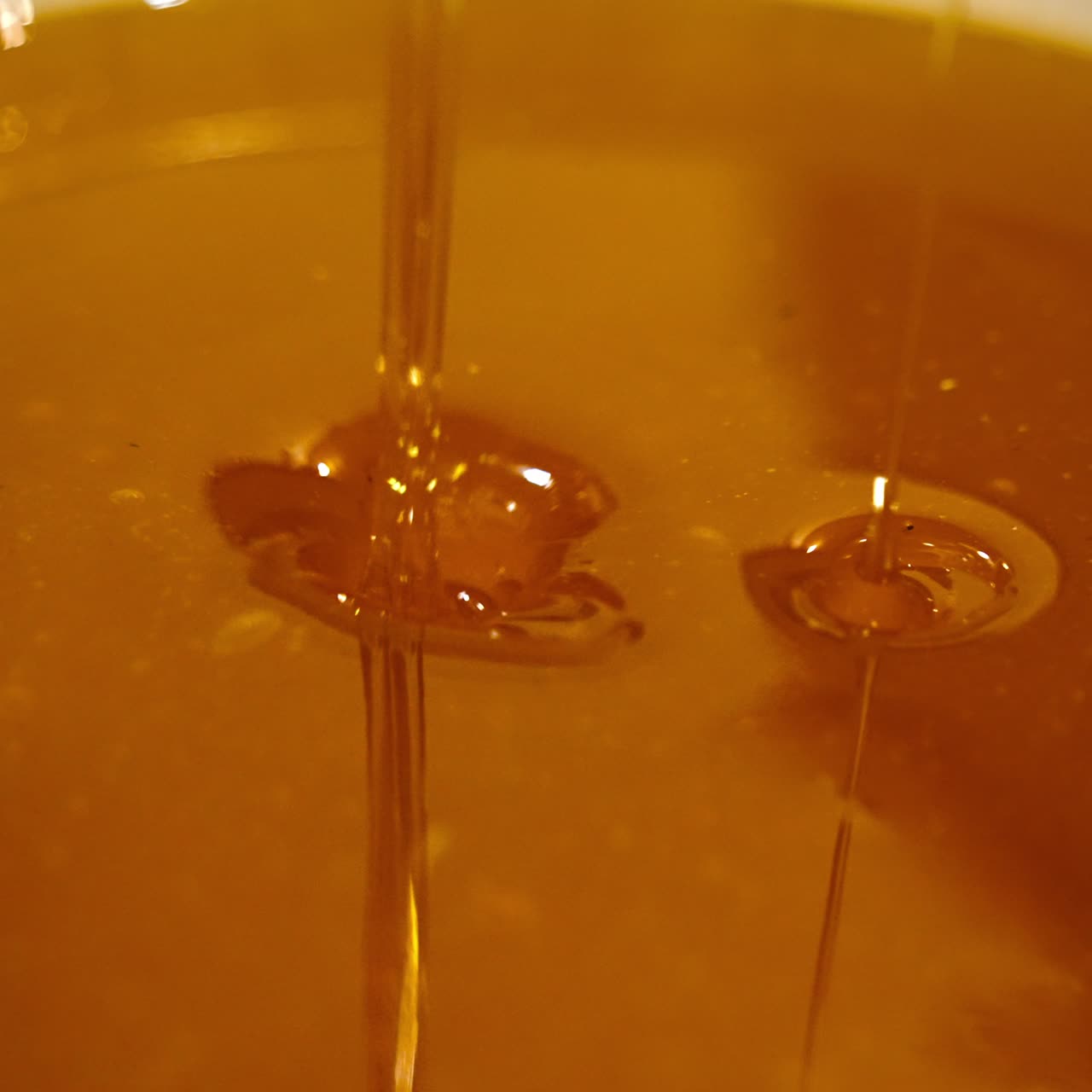 Miele liquido dorato appena raccolto in una ciotola. Piccoli rivoli che riempiono il recipiente. Concetto di cibo naturale, biologico e sano, da vicino.