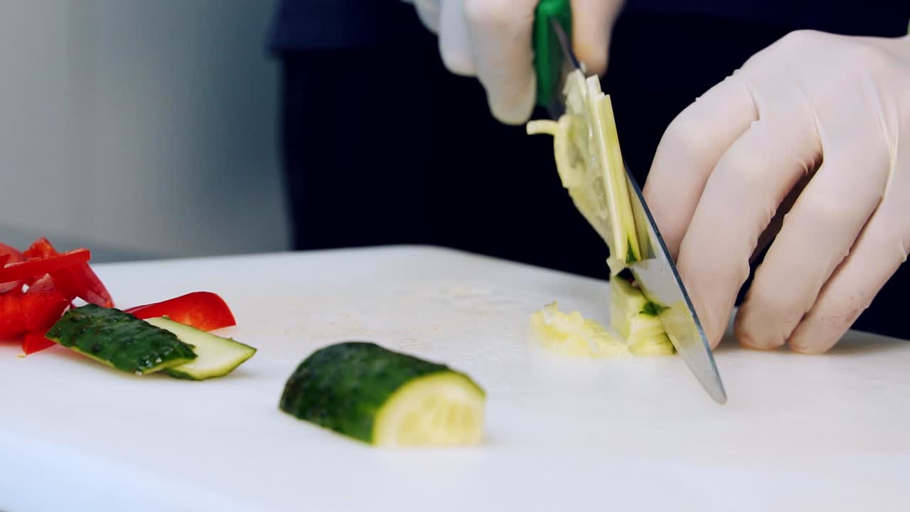 Process of slicing a cucumber. Chef's hands in gloves cut fresh cucumber on kitchen table. Tasty organic food ingredients. Healthy diet nutrition