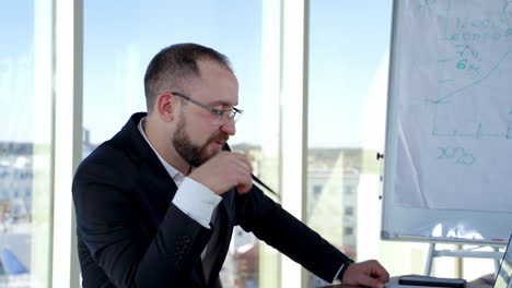 smiling business worker talking to someone in office. portrait of entrepreneur in glasses and costume sitting at his desk on the background of window in the city.