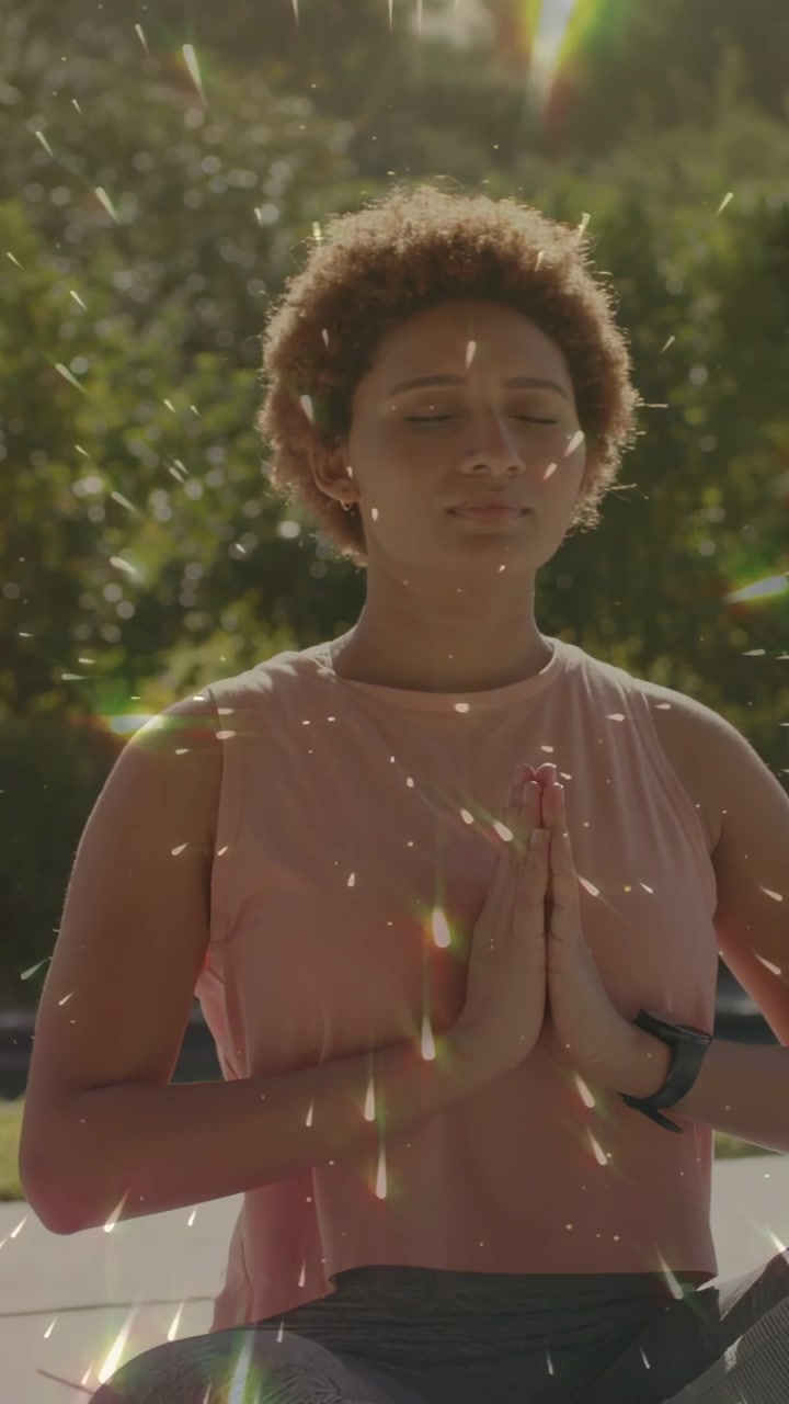 Video verticale: Donna che inspira, alza i palmi e li abbassa al petto, seduta per lo yoga, con il sole che le brilla addosso.