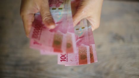 Woman-counts-many-rupiah-Red-100,000-banknotes-in-hands-with-wooden-background