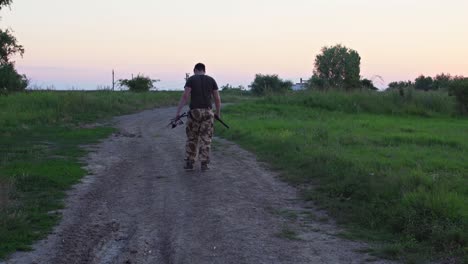 back view of a man with farming tools walking on dirt road through fields at sunset
