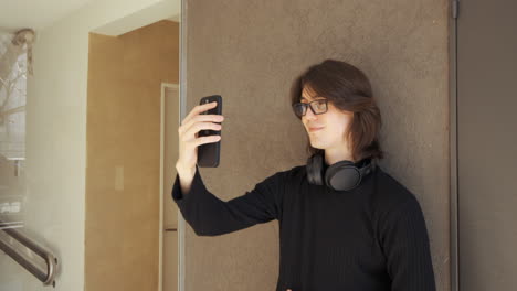 young man with glasses on a video call using his mobile phone, headphones around his neck