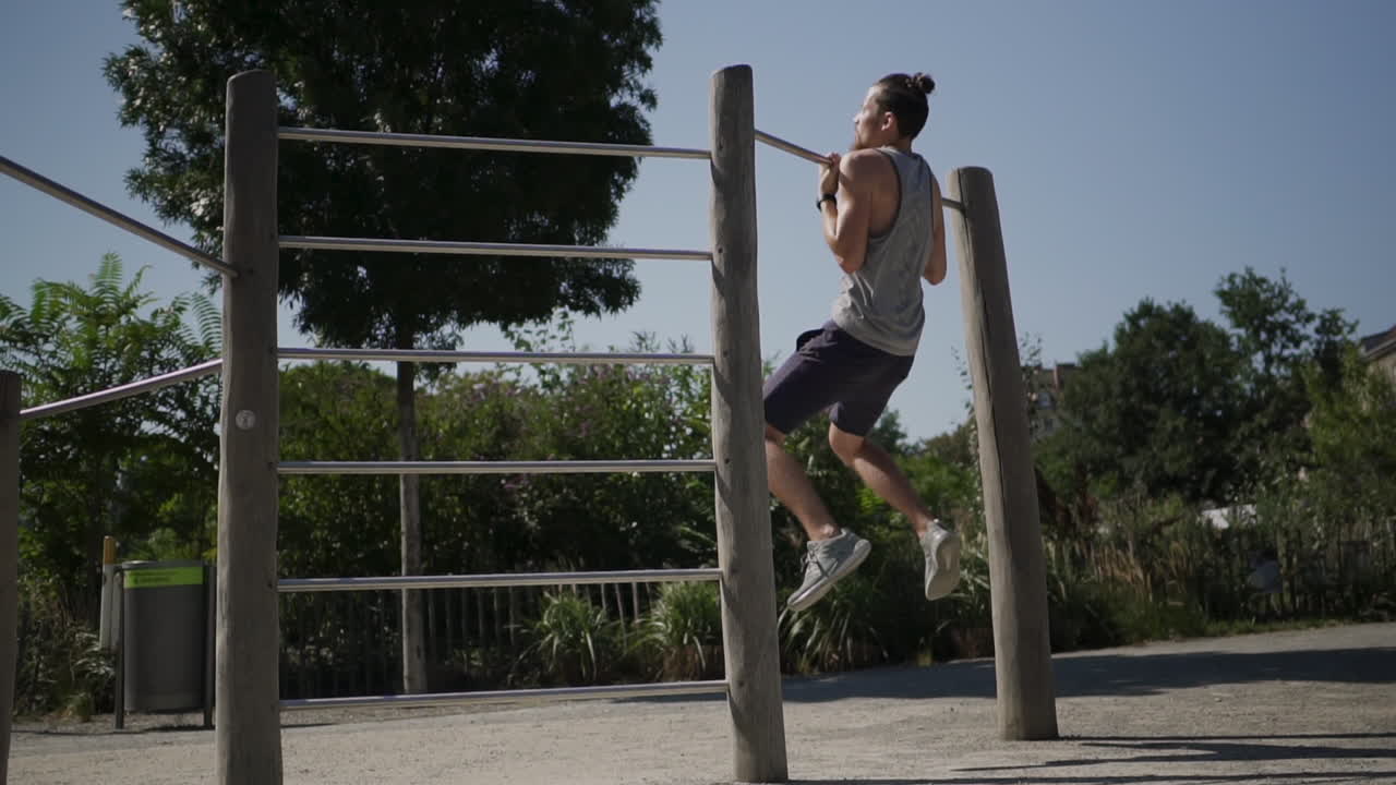 hombre realizando un movimiento lento tirando hacia arriba desde atrás durante un entrenamiento en un parque