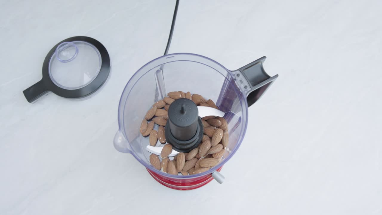 Hand adds almonds into blender from top view during food preparation