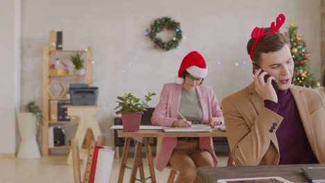 Young-Serious-Businessman-In-Xmas-Headwear-Talking-On-The-Phone-While-Planning-Work-Sitting-In-Front-Of-Laptop-On-Christmas-Eve