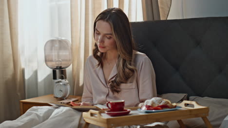 woman having breakfast in bed while reading