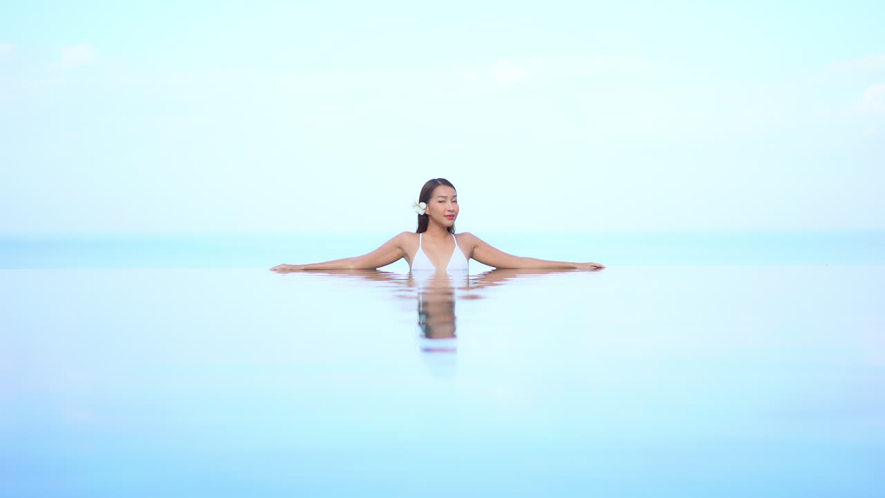 misteriosa mujer asiática sexy dentro de la piscina infinita girando lentamente su vista hacia la cámara en el simplista fondo del cielo, plantilla