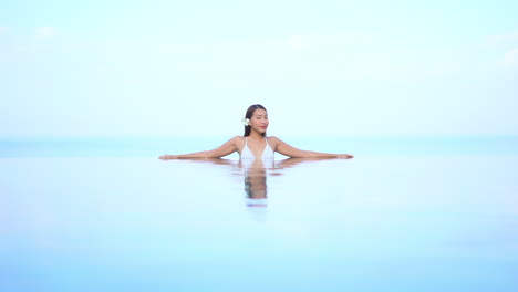 misteriosa mujer asiática sexy dentro de la piscina infinita girando lentamente su vista hacia la cámara en el simplista fondo del cielo, plantilla