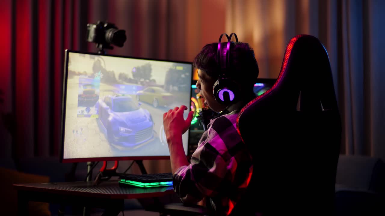 Back View Of Asian Boy Streamer Playing Car Racing Game Over Network On Personal Computer. Yawning And Sleeping, Live Stream Video Game, Desk Illuminated By Rgb Led Strip Light