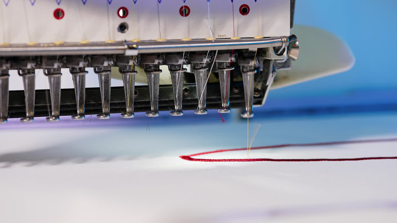 Automatic embroidery machine is working. Sewing machine needle in motion. Sewing machine needles with different colors moves up and down on white fabric. Close-up.