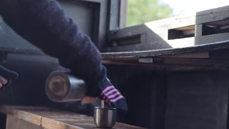 Woman-pouring-a-flask-of-hot-coffee-in-nature-hide