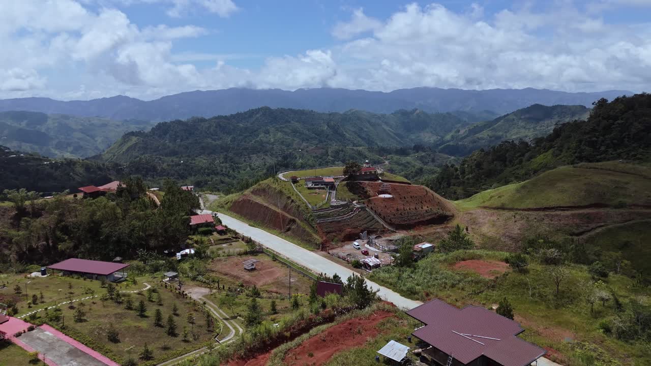 Wide drone panorama of scattered vacation cabins and mountain resorts on rolling hills in Marilog District. Scenic highland landscape with distant mountain ranges under a blue sky in Davao