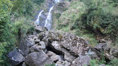 Wasserfall-In-Asien,-Kamerafahrt-Mit-Vielen-Pflanzen-Und-Steinen-Im-Vordergrund