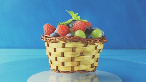 rotating wooden basket with different forest berries close-up on a blue wooden table. 4k slow motion loop video with speed ramp effect.