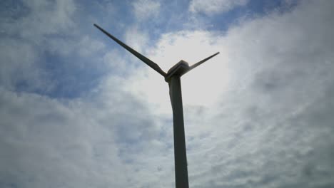 Wind-turbine-rotating-against-bright-cloudy-sky-with-sun-breaking-out