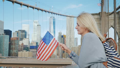 young tourist with a flag of america and a backpack standing on the brooklyn bridge on the backgroun