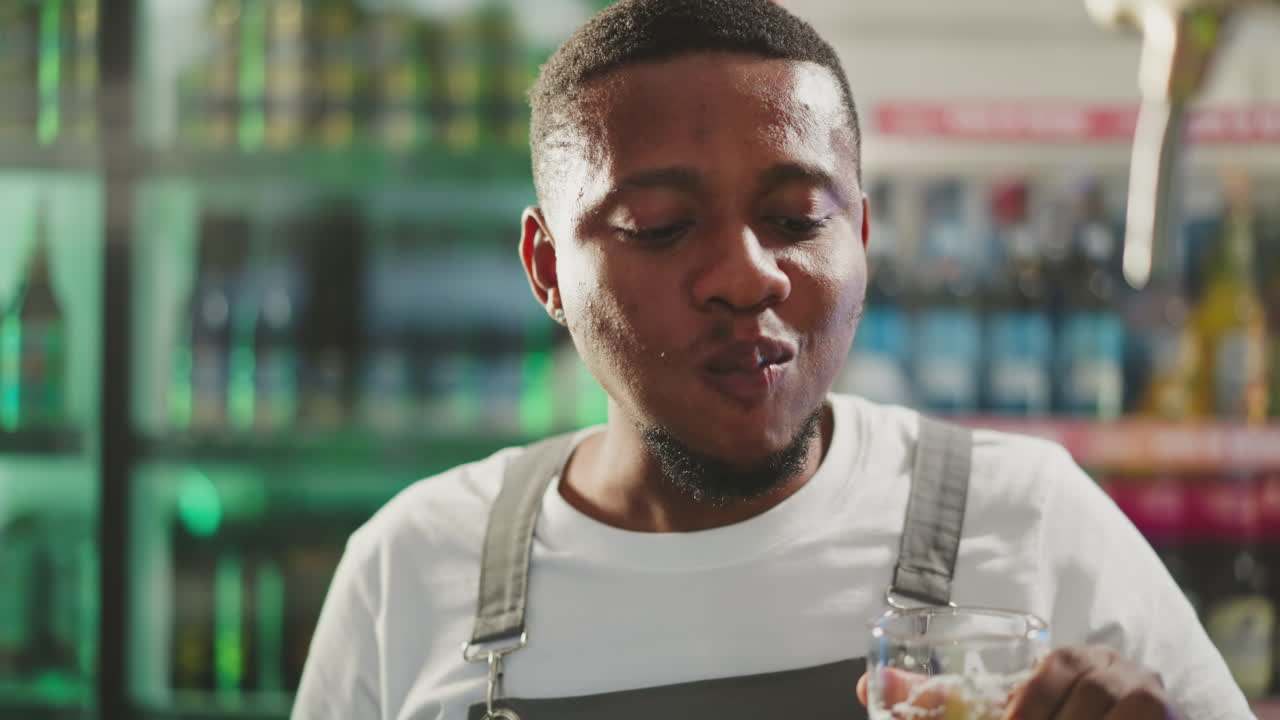 Black man degustates beer with satisfaction in pub closeup. African American brewer checkups taste of light alcohol drink working in bar. Craft brewery owner
