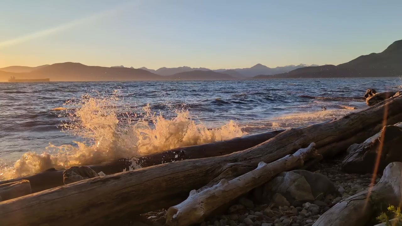 Starke Wellen, die am Strand brechen und Baumstämme herumtreiben. Kanada Vancouver Sonnenuntergang Abendstimmung.