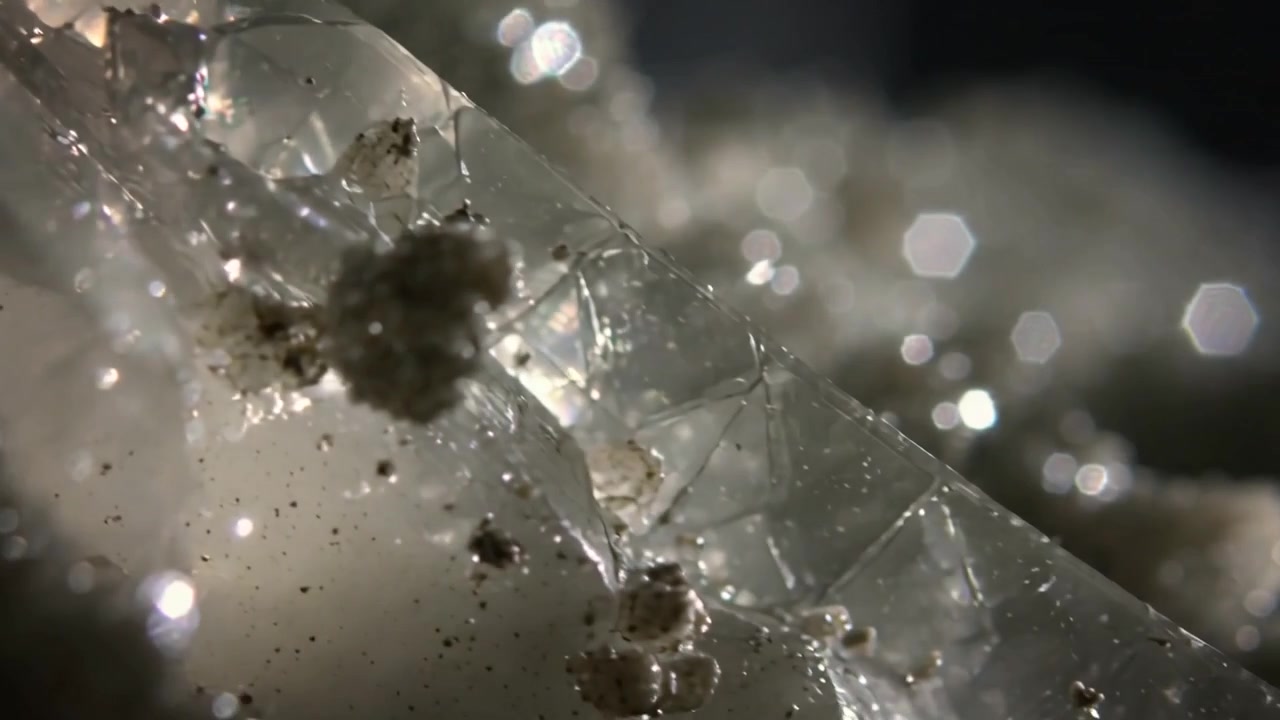 Caméra en mouvement révélant un cristal clair en macro, exposant les facettes, les sédiments et le bokeh pour le détail.