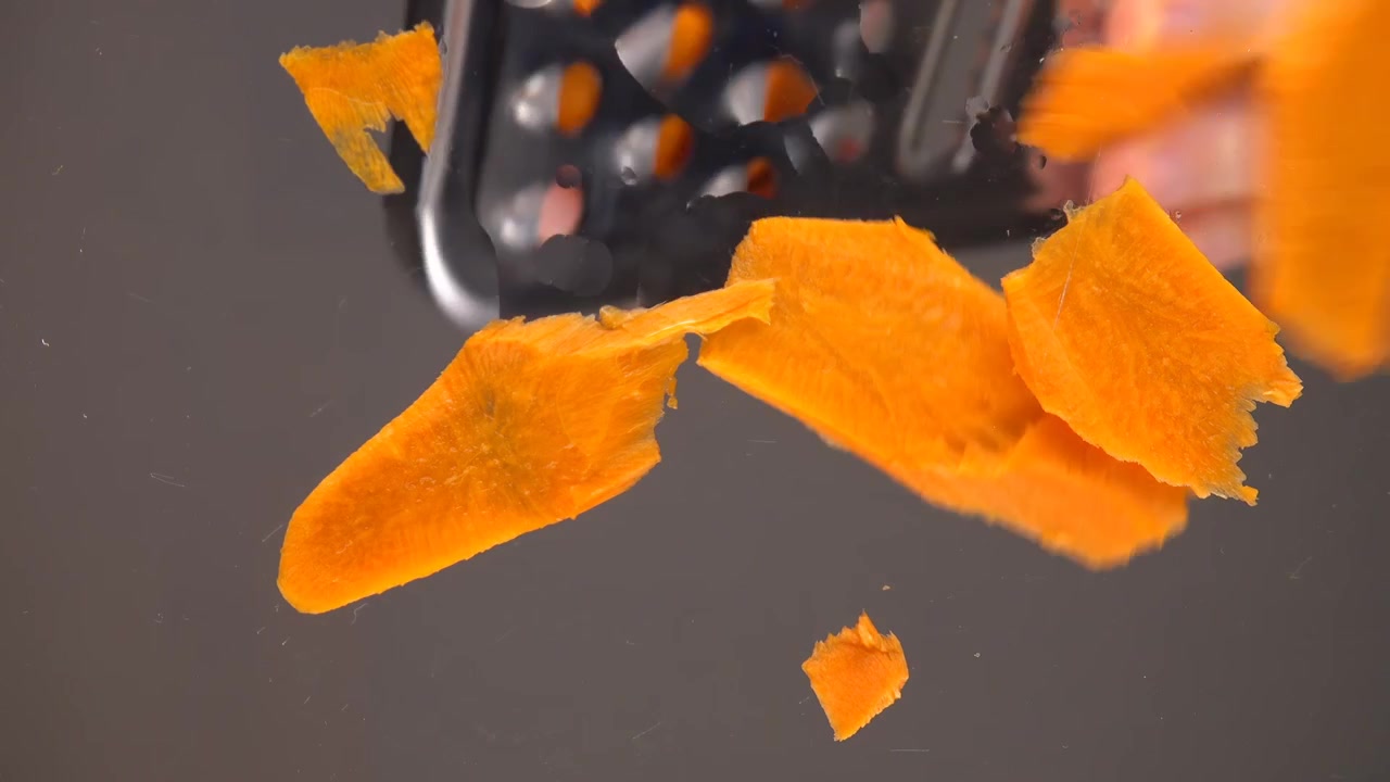The cook rubs raw carrots into a glass dish. Bottom view.