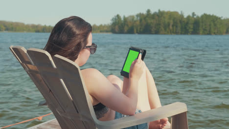 la cámara se desplaza sobre una mujer que se relaja en un muelle junto a un lago en la temporada de verano con una pantalla verde para la clave de croma