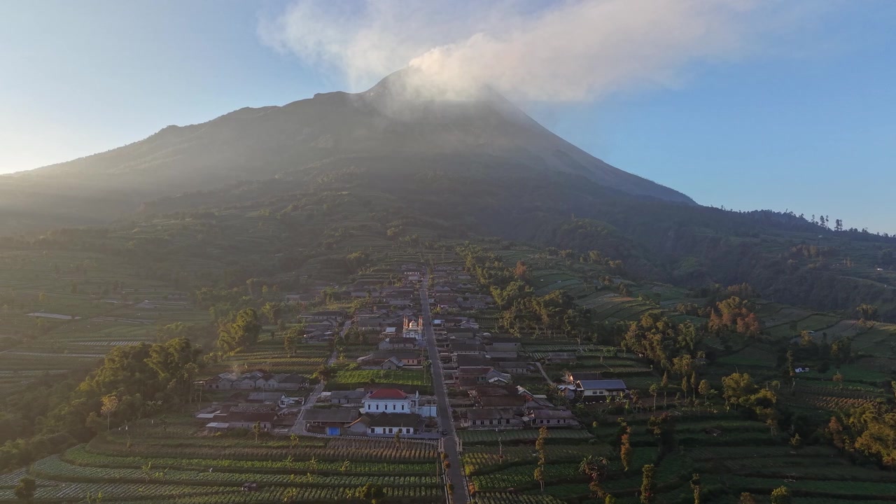 Riprese aeree panoramiche di un villaggio rurale sotto il Monte Merapi. La vegetazione lussureggiante e il terreno vulcanico mostrano la bellezza naturale dell'Indonesia.