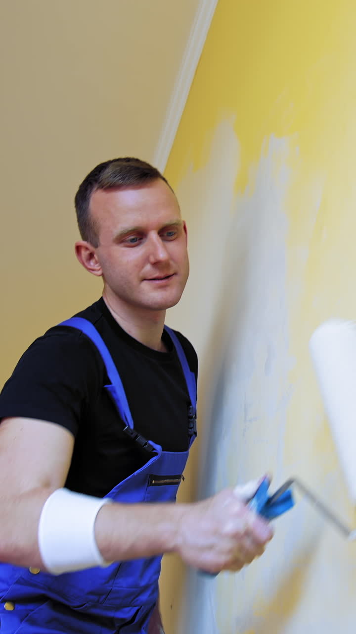 Attractive painter doing new interior of wall. Cheerful man working with paintings. Vertical video