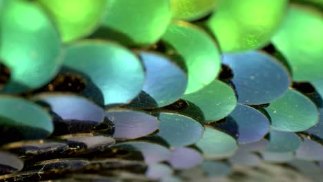 moving very slowly across a segment of brightly colored blue, teal, and green sequins moving top to bottom