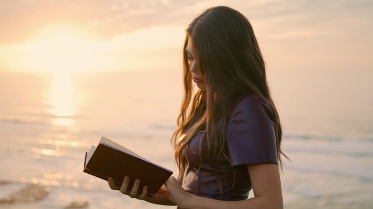 Girl reading book sunset close up. Brunette holding foliant standing at seashore