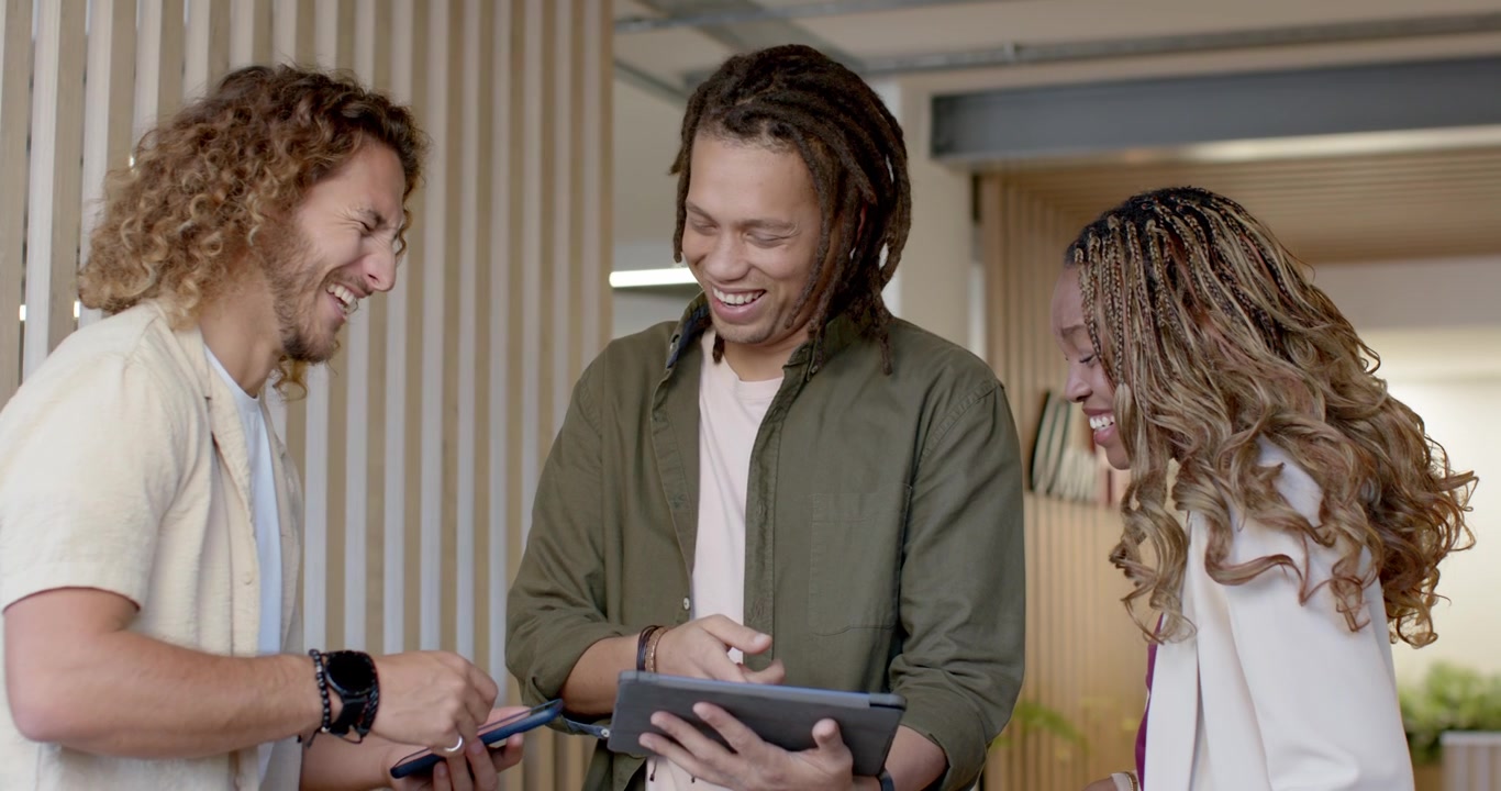 Mangfoldigt team gennemgår indhold på en gang, hvor en person til venstre peger på en telefon, og en i midten stryger på en tablet og griner.