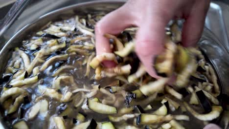 chef is washing sliced aubergines inside a pot full of water. slow motion