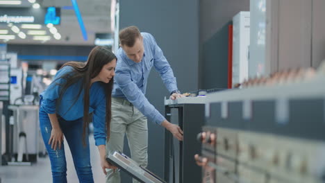 the man and the woman to open the door of dishwasher appliances in the store and compare with other models to buy the new house