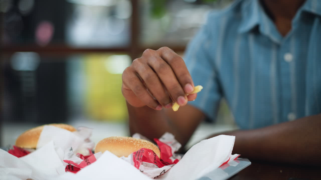 Blurry close view of hand holding fries near blue shirt in open bright space, shallow depth of field creating soft background, suggesting casual snack moment and relaxed atmosphere