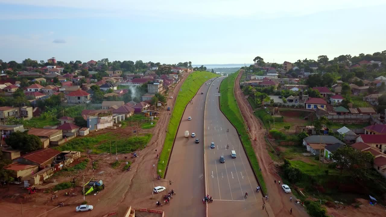 autopista kampala-entebbe, uganda, áfrica oriental - vehículos que viajan en la carretera que limita con una zona residencial - avión no tripulado volando hacia adelante