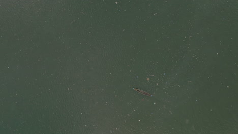 wide aerial top down overview of canoe moving amongst the trash in the water