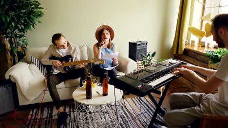 amateur band is rehearsing in home studio singing and playing guitar and keyboard using microphone and musical equipment. beer bottles and snacks are visible.