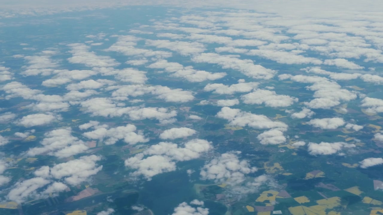 飛行機の窓から見た空撮の白い雲の風景、追跡ショット。緑豊かな地形の上に広がる積雲の絨毯を見下ろす、60fpsの高高度からの乗客視点。