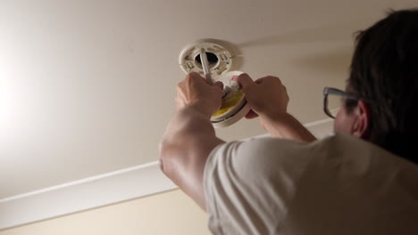 el hombre vuelve a conectar el cable eléctrico a un detector de humo después de reemplazar la batería de la alarma