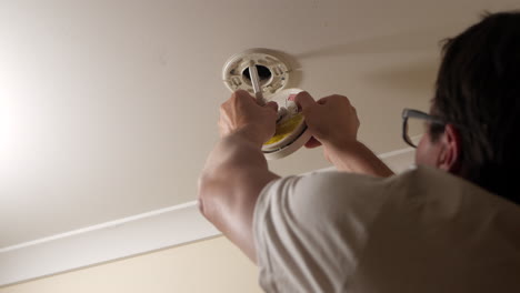 man reattaches electrical cord to a smoke detector after replacing the alarm's battery