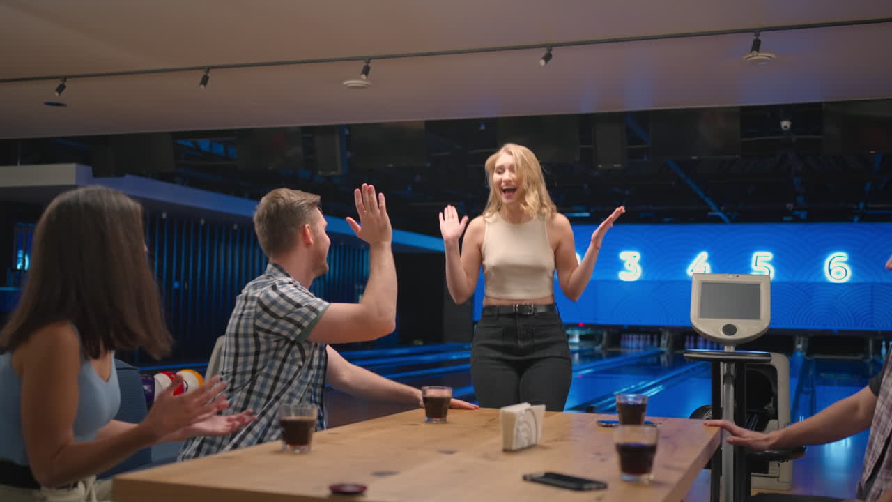 Donna felice in una sala da bowling corre gioiosamente dalle sue amiche per festeggiare la serie di strike. Condividi la vittoria con gli amici. Gruppo di amici multietnico.