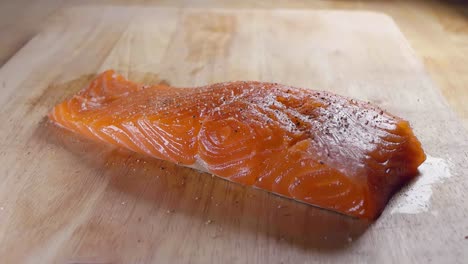 cerrar toma en cámara lenta de sazonar un trozo fresco de filete de salmón con sal antes de cocinar en la cocina