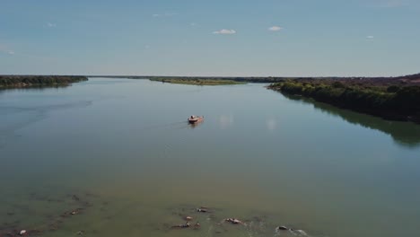 wide aerial shot following a small ferry sailing on the sao francisco river in rural brazil