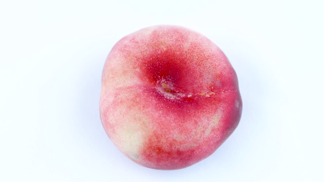 Tampilan atas dari satu buah persik pipih donat. Berputar di meja putar terisolasi dengan latar belakang putih. Close-up. Makro.