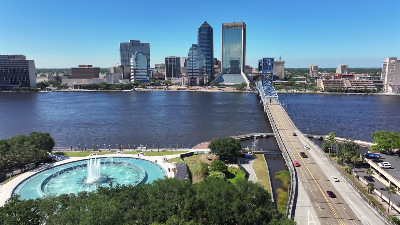 Aerial lateral shot of fountain and driving cars on John T. Alsop Jr. Bridge with downtown in background. Sunny day with blue sky and skyline. Wide shot.