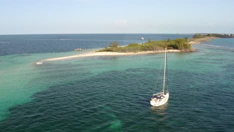 sailboat floating in shallow sea water with beautiful coral reef at the bottom and tropical paradise island in background