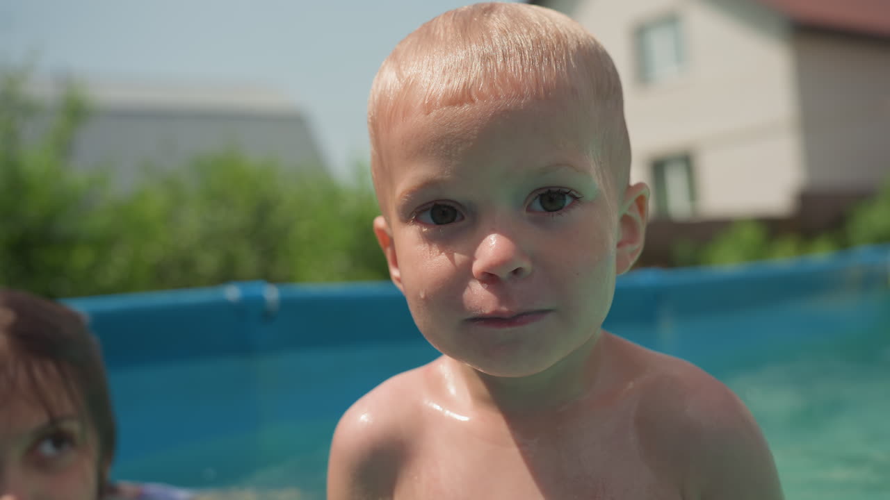 Young Kid Scrutinizes Camera Closely, Child By Pool Fixes Attention On Camera With Serious Expression, Young Child Standing Near Water With Intense Focus Directed Towards Camera Viewfinder
