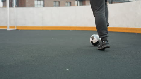 leg view of individual skillfully dribbling soccer ball on sport arena surface during training session, demonstrating precision and agility, background includes chain-link fencing and blurred goal