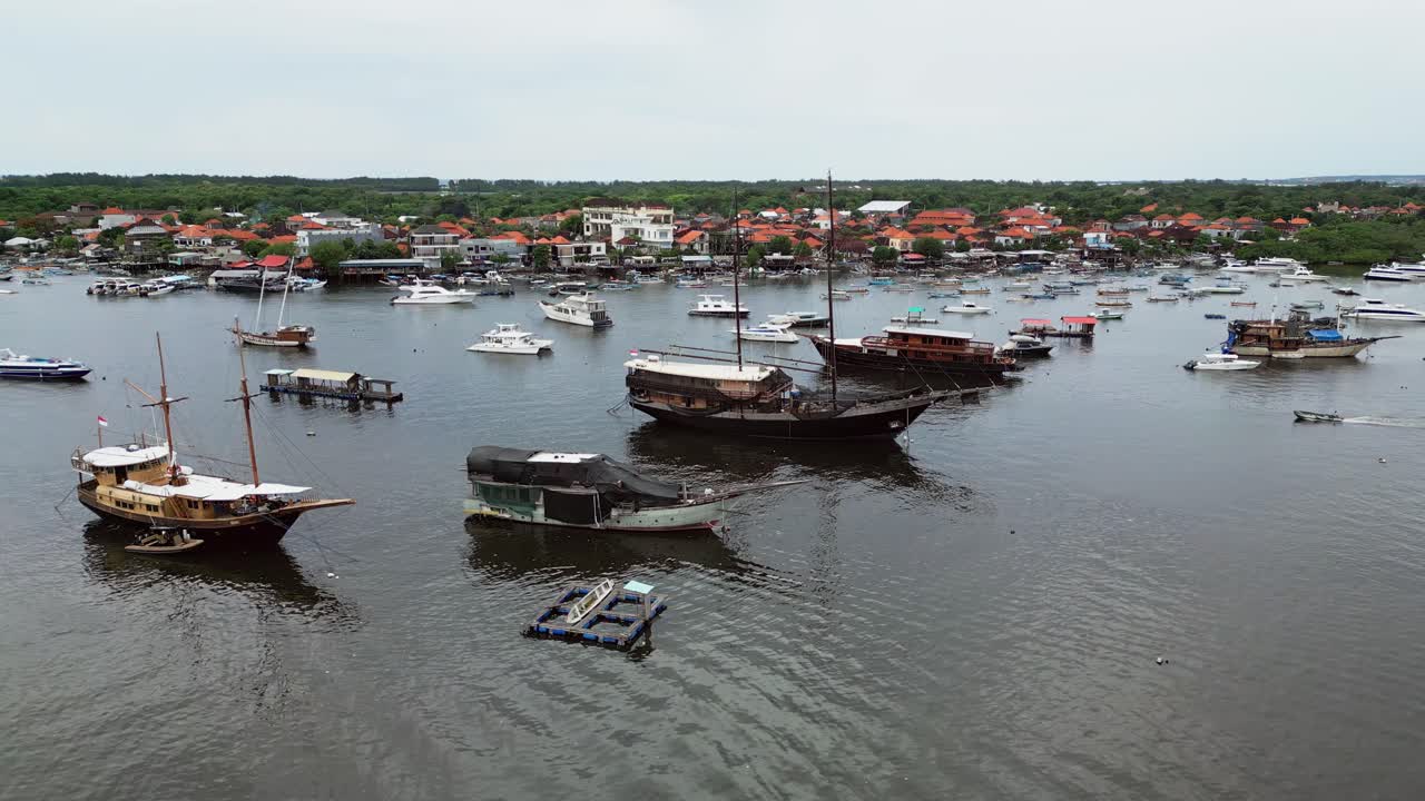 Luftaufnahme von traditionellen hölzernen Segelbooten, die in einem ruhigen Küstenhafen liegen, umgeben von ruhigem Wasser und Gebäuden an der Küstenlinie, die die maritime Kultur und die tropische Küstenatmosphäre hervorheben