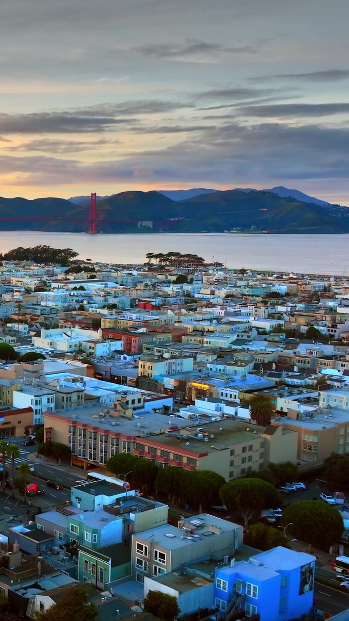 Vista distante del Golden Gate Bridge sul quartiere Marina, San Francisco, California. La luce del crepuscolo si diffonde sull'acqua della baia, sulle colline e sui tetti costieri. Video verticale